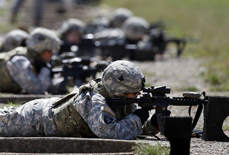 Soldiers lie on the ground firing guns