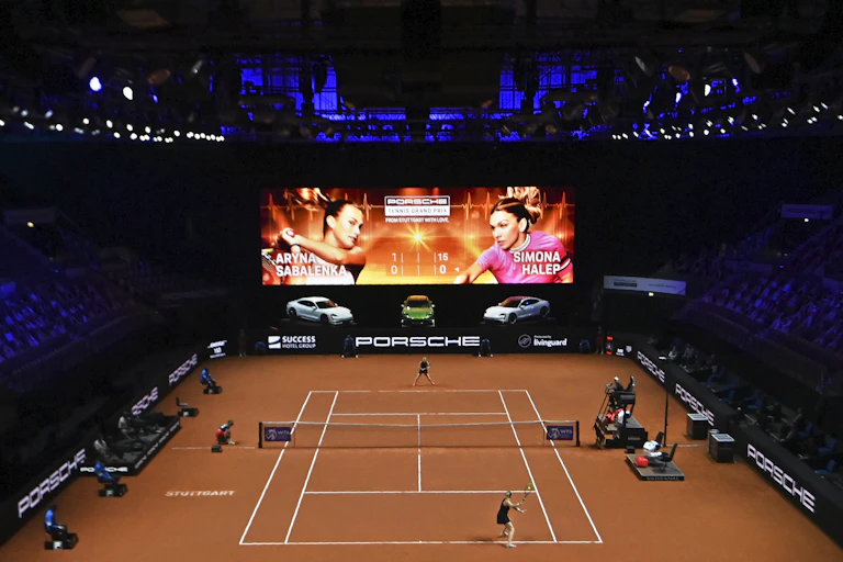 Tennis court with empty spectator seats, wide shot, two women playing