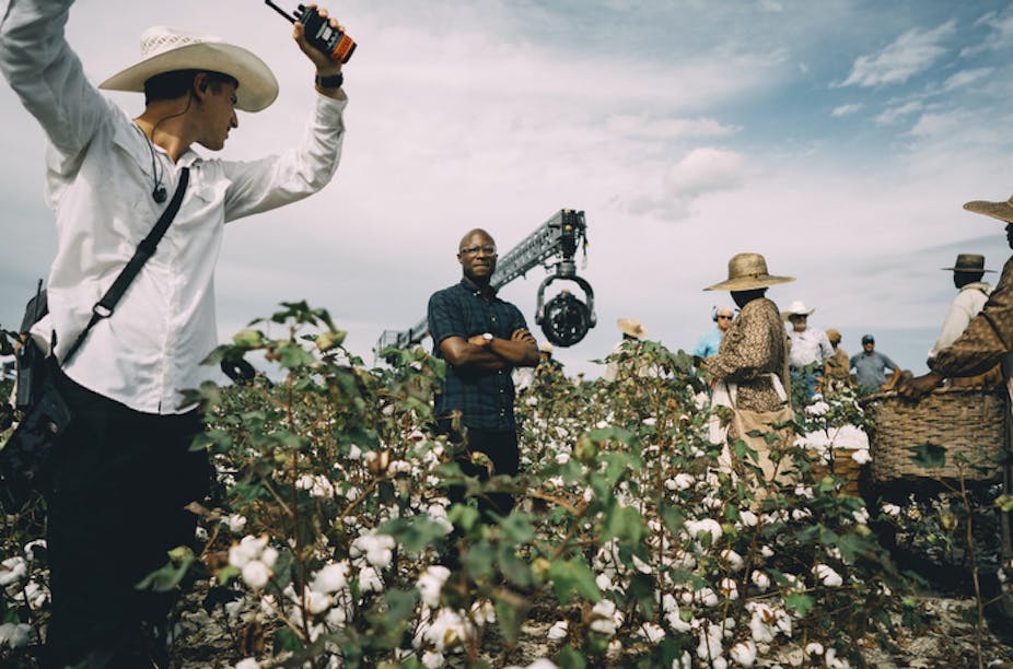 Barry Jenkins stands, arms folded, in a cotton field, surrounded by crew and cast.