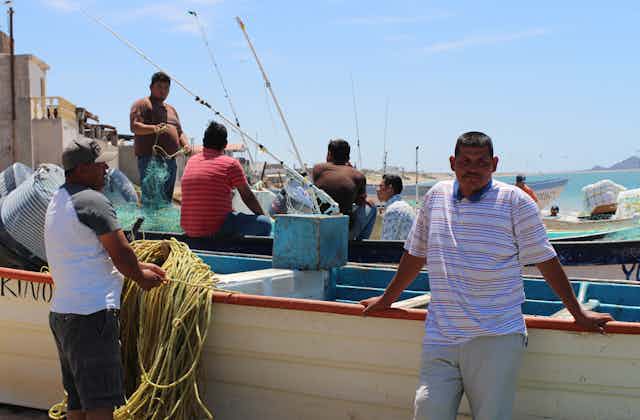 A group of men standing near boats with fishing rods.