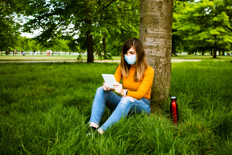 A woman reads outdoors with an e-reader.