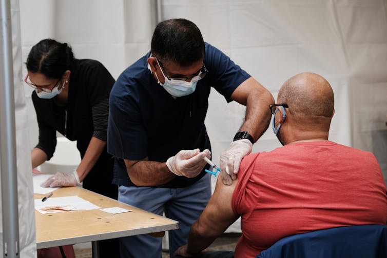 A man gives a shot to another man at a vaccination center.