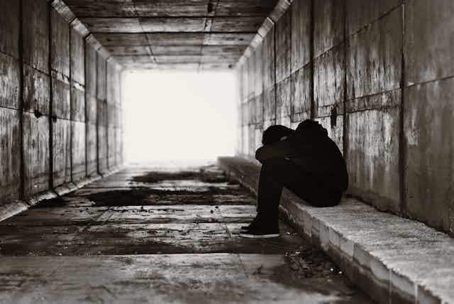 Teen huddled over sitting on bench in underpass