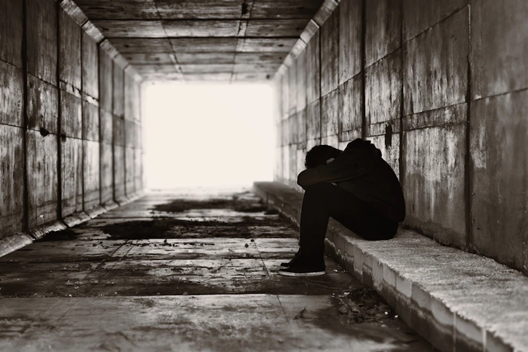 Teen huddled over sitting on bench in underpass