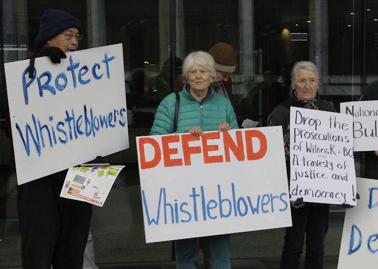 Protesters hold signs saying 'defend whistleblowers'.