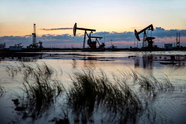 Oil derricks on a wetland horizon at dusk.