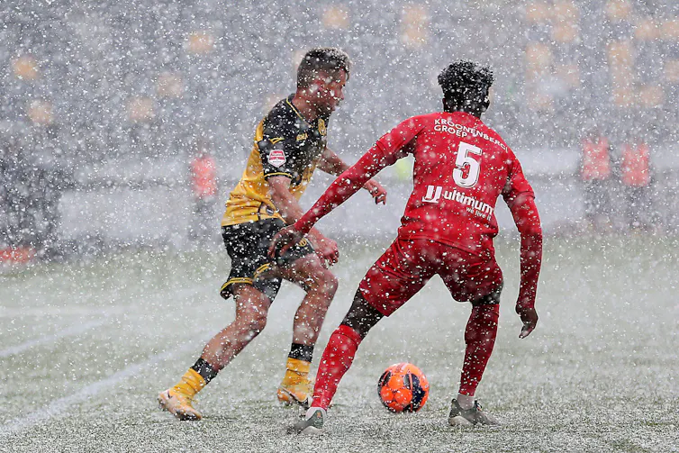 Two football players in stadium with snow falling