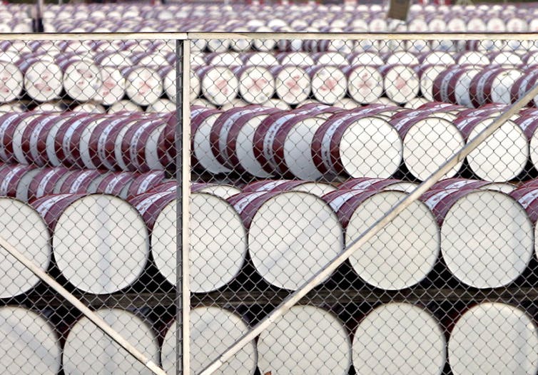 White-bottomed barrels piled in rows behind a chainlink fence.