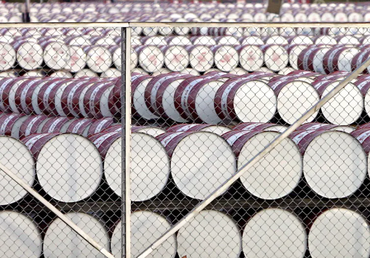 White-bottomed barrels piled in rows behind a chainlink fence.