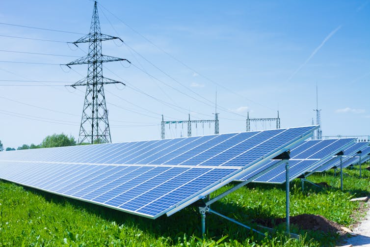 A row of ground-mounted solar panels with a pylon in the background.