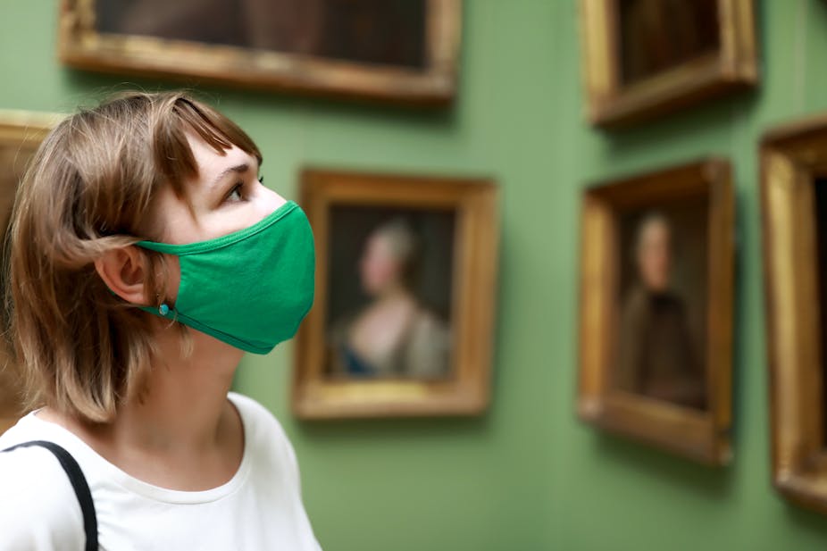 Woman in green masks looks at artwork.