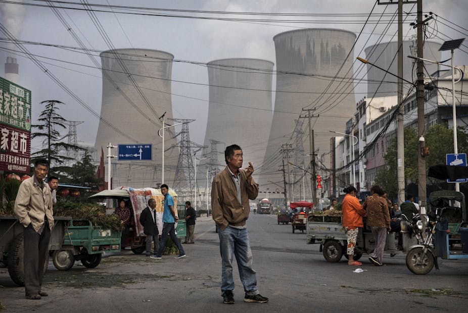 A man smokes in a street market with a coal-fire power plant in the distance
