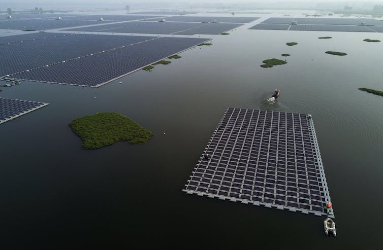 A boat pulls a large section of solar panels into place among others on the large lake.