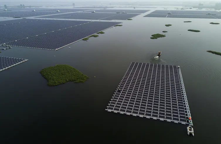 A boat pulls a large section of solar panels into place among others on the large lake.