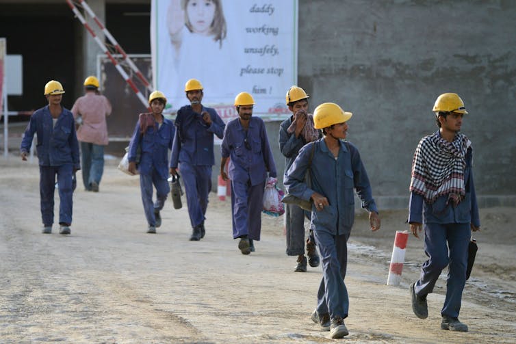 Construction workers in hard hats pass a sign urging them to work safely