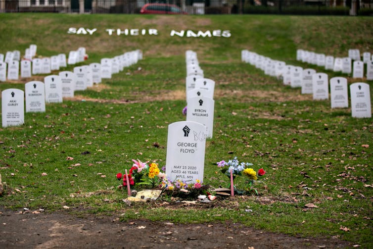 George Floyds headstone sits front and center in an orderly faux cemetery with other white headstones set up in grass