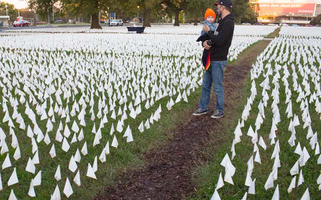 man holds a baby in a field of tiny white flags