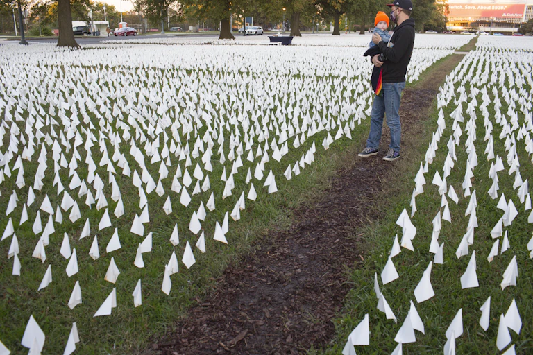 man holds a baby in a field of tiny white flags