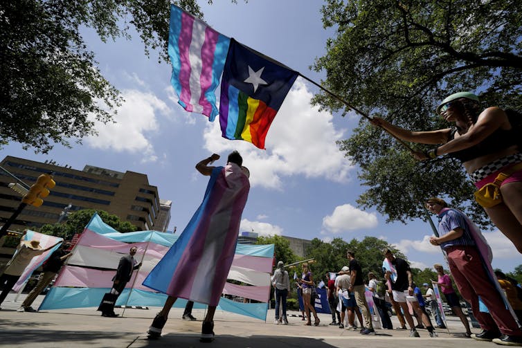 Demonstrators stand with a trans flag in the street.