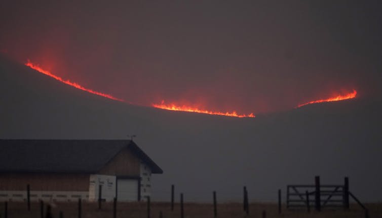 Fire lights up a ridge behind a farm.