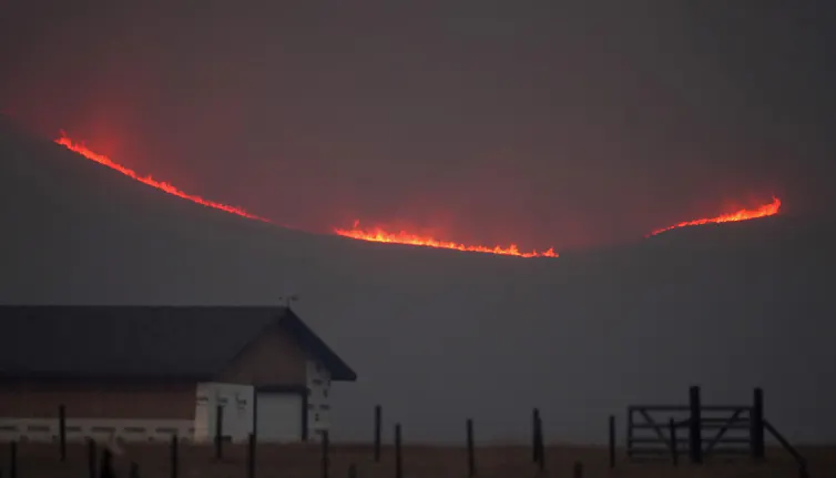 Fire lights up a ridge behind a farm.