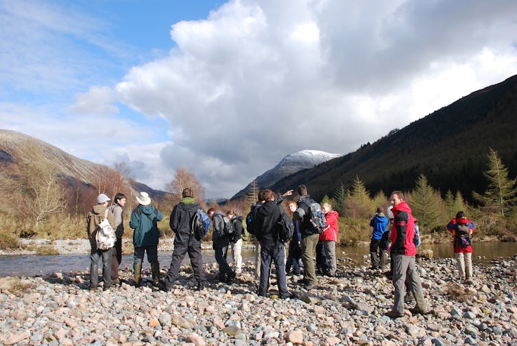 A group of people standing in a valley bottom surrounded by trees and hills.