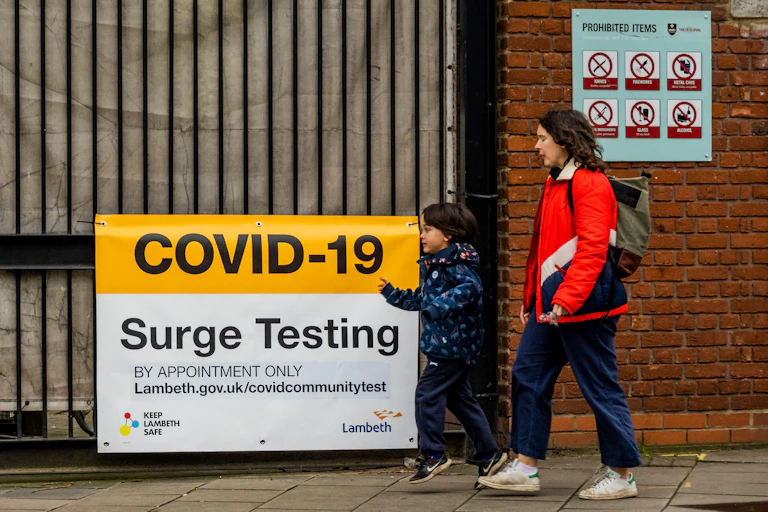 Mother and child walking past a COVID-19 Surge Testing sign in Oval, London.