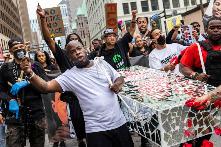 Protesters carry a cardboard coffin down a city street