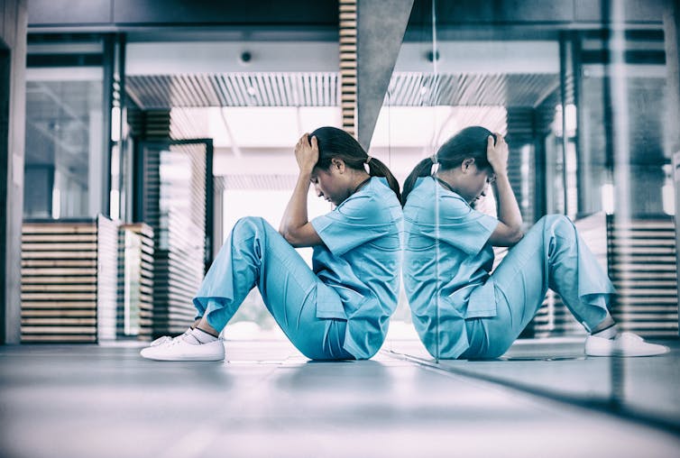 A health care worker sits on the floor and holds her head