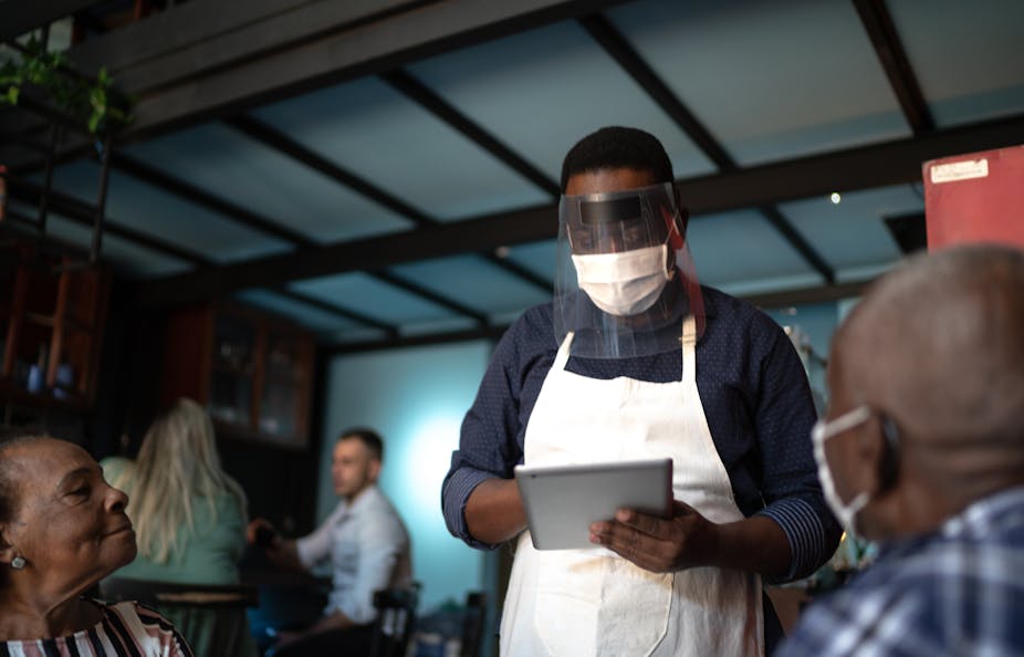 Masked waiter taking an order in a restaurant.