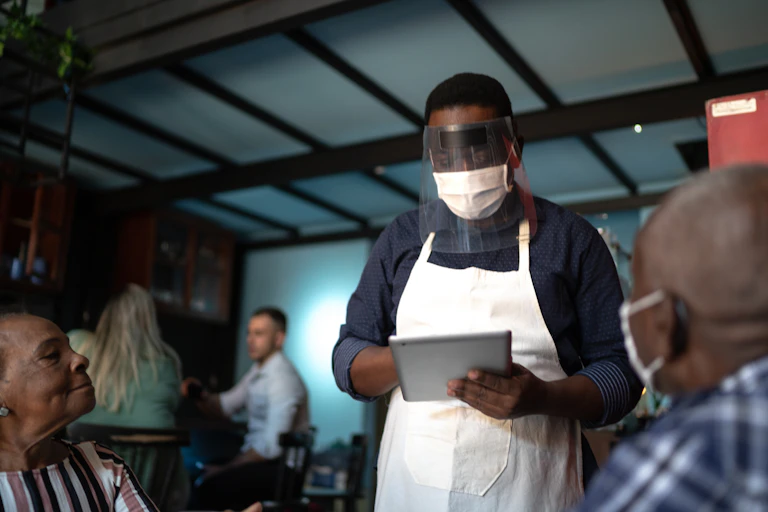 Masked waiter taking an order in a restaurant.