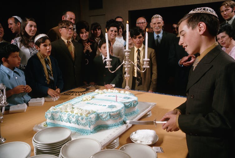 A Jewish boy cuts a cake for family and friends after his bar mitzvah ceremony.