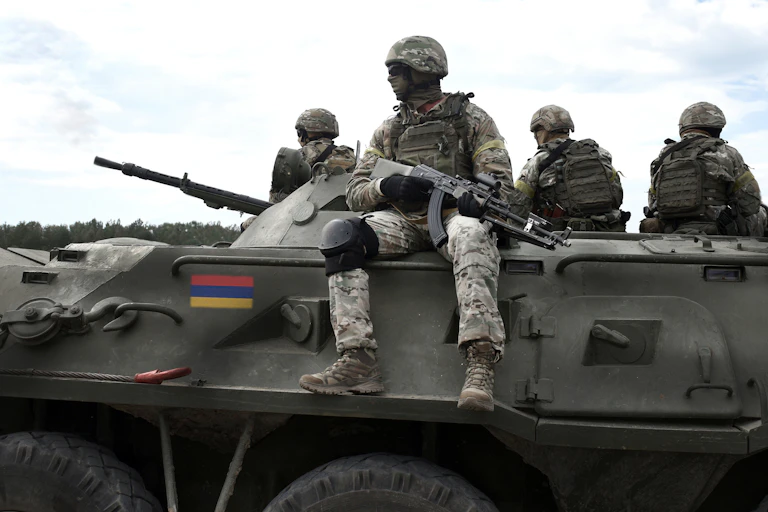 Armed Armenian troops sitting on top of an armoured personnel carrier with an Armenian flag.