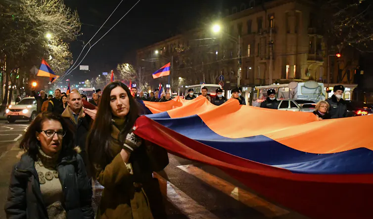 Women and men carrying a giant red, blue and orange flag through the streets at night.