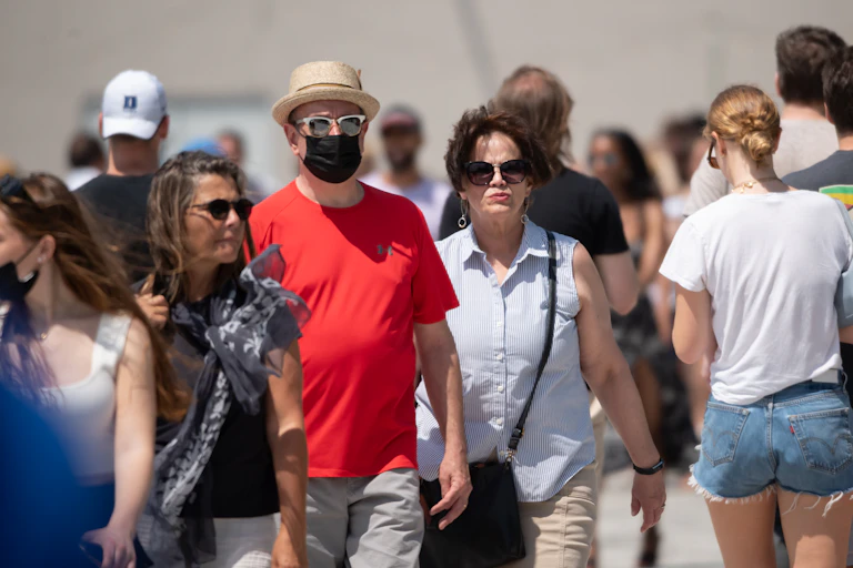 people walking outside, one man has a mask on