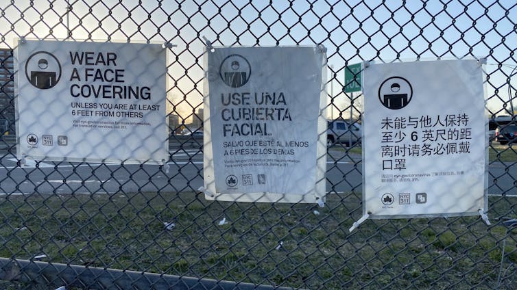 coronavirus precaution signs in multiple languages hang on a fence