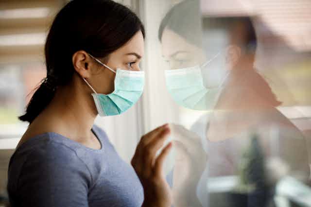 Woman wearing a face mask looking closely out a window.