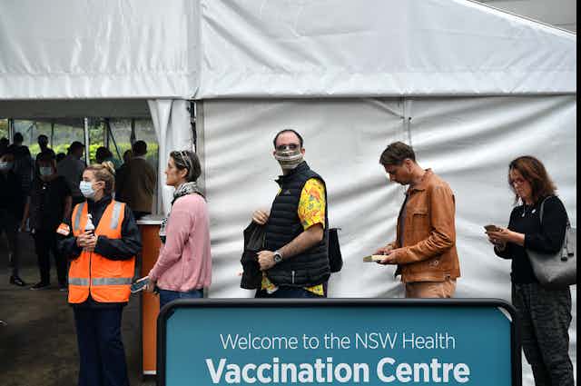 People queueing alongside a sign which reads 'Welcome to the NSW Health Vaccination Centre'.
