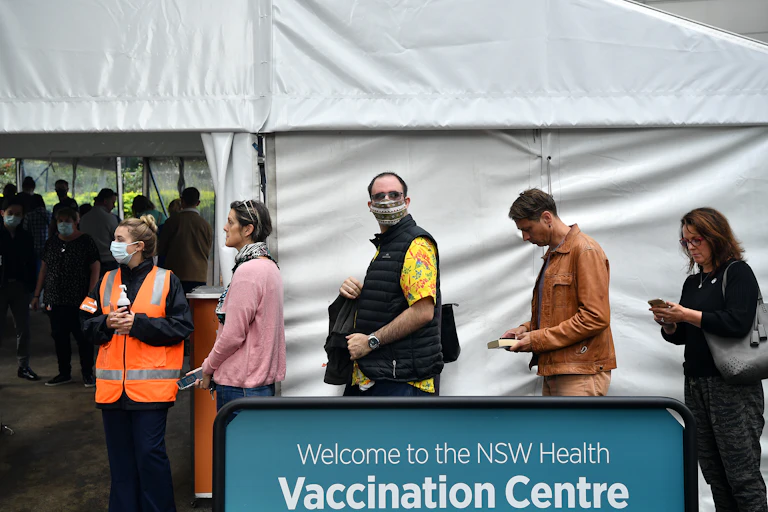People queueing alongside a sign which reads 'Welcome to the NSW Health Vaccination Centre'.