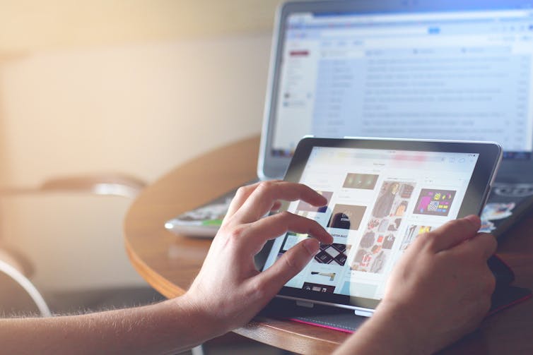 Hands using a tablet in front of a laptop