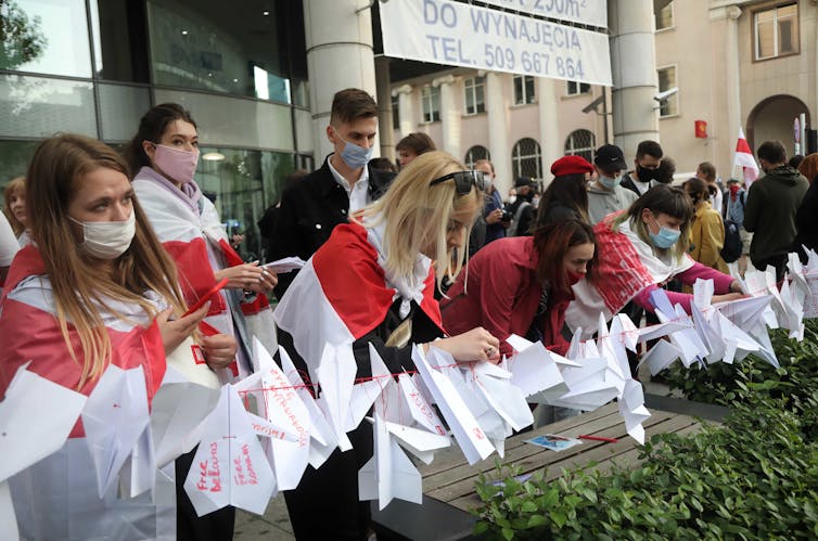 Women wearing capes made from the red and white flag of the Belarusian opposition making paper planes.