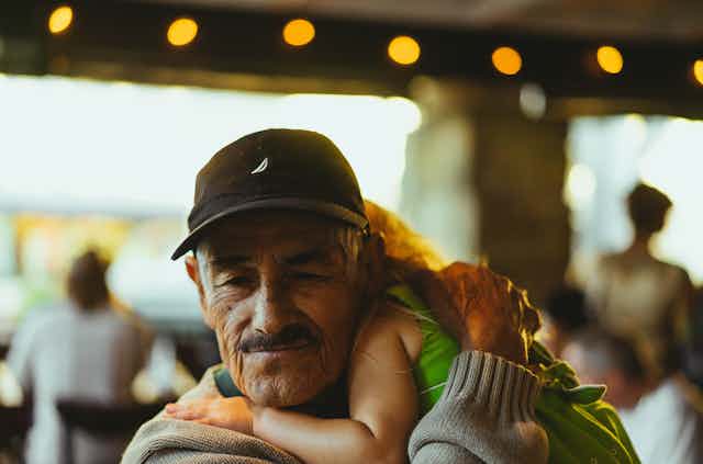 A grandfather wearing a ballcap cuddles his grand-daughter.