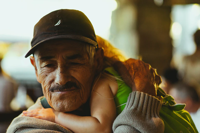 A grandfather wearing a ballcap cuddles his grand-daughter.