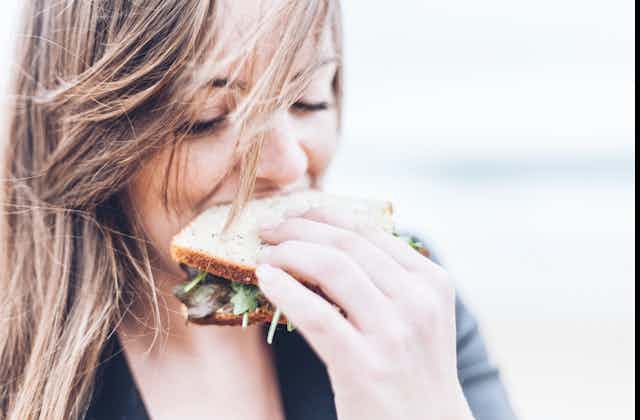 A woman takes a bite of a sandwich.