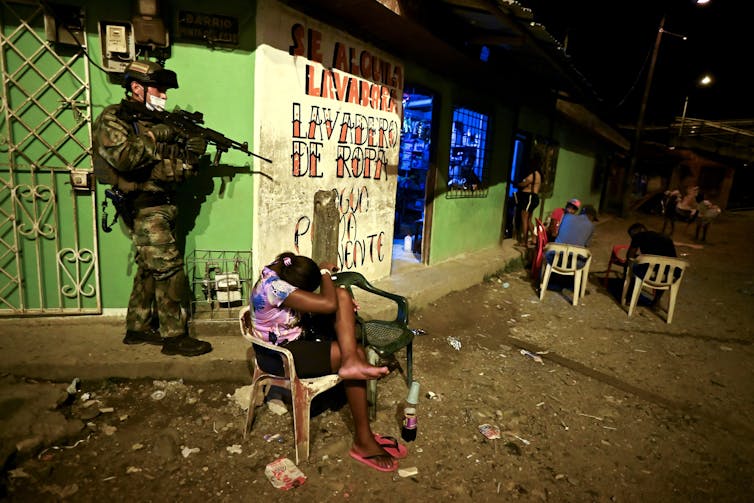 Soldier in fatigue holds a weapon while a young girl covers her head