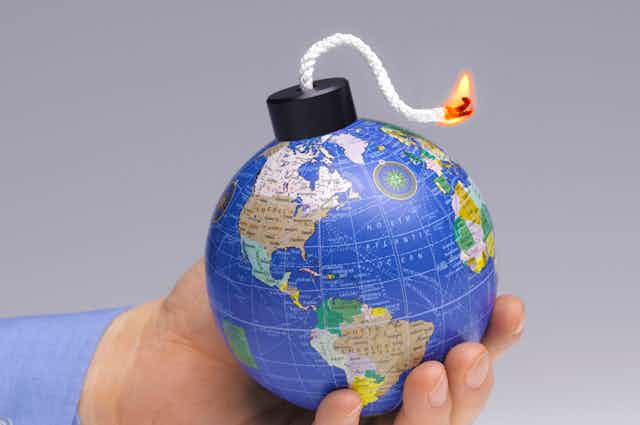 A hand holding a small globe with a lit fuse.