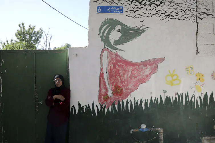 A woman stands beside a large mural of a young girl in a red dress