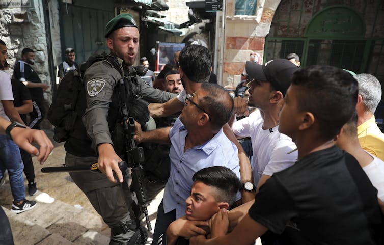 A police officer pushes away a crowd that includes a young child