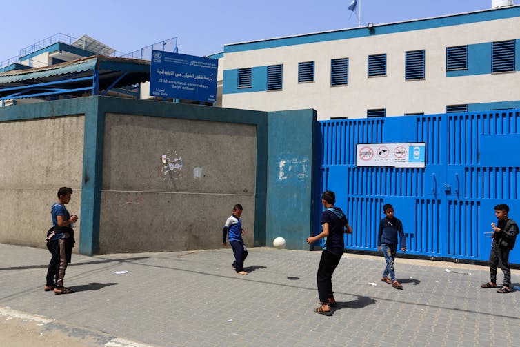 Boys playing football outside closed school gates in Gaza