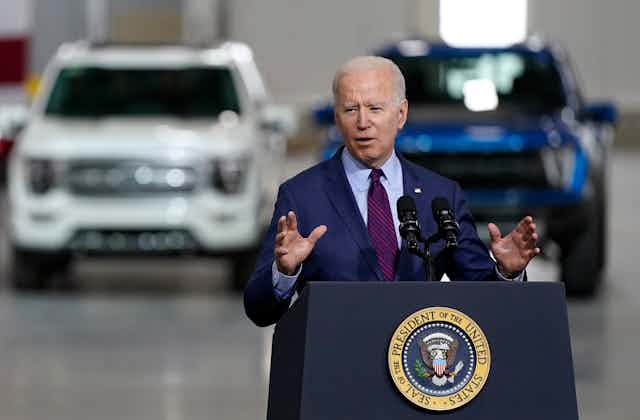 President Biden speaking in front of two electric SUVs at a factory